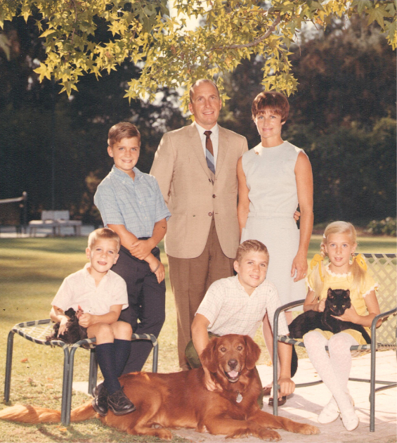 A vintage color photo shows a family with two parents and four children, plus pets, standing outside in the fall.