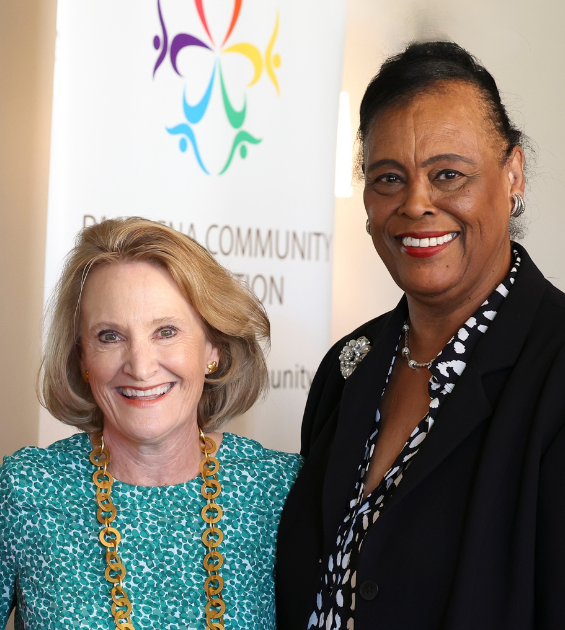 Two older women stand together with a banner behind them