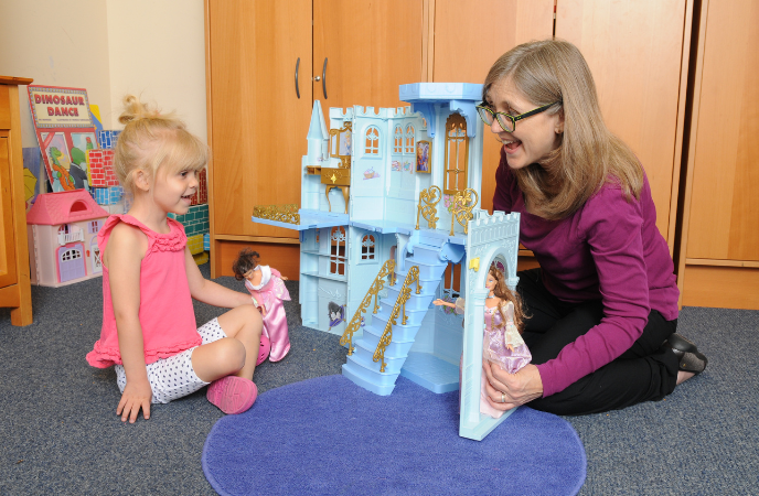A woman plays with a young girl on the floor with a large blue castle and dolls