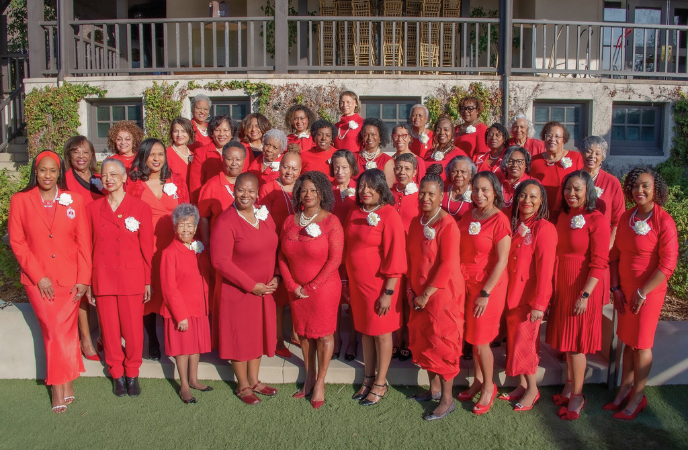 A large group of African American women, all wearing red suits, stand in four lines facing the camera