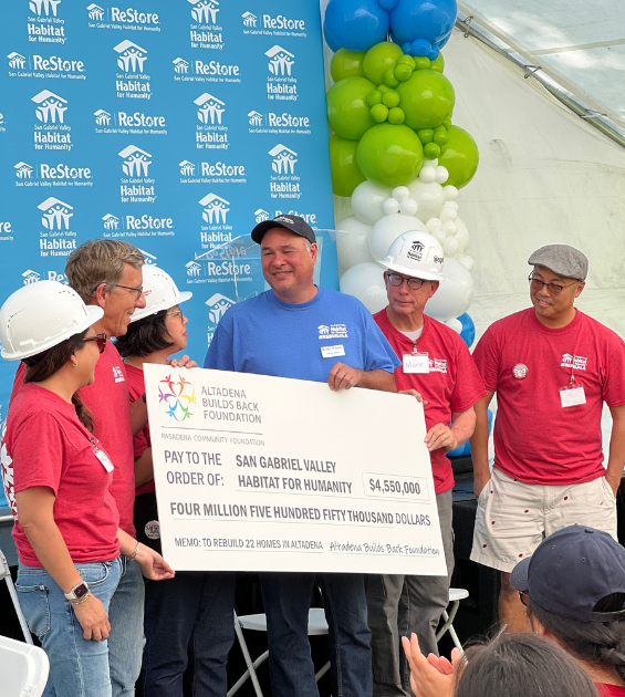 A group of people wearing hard hats presents a big check to a Habitat for Humanity staff member