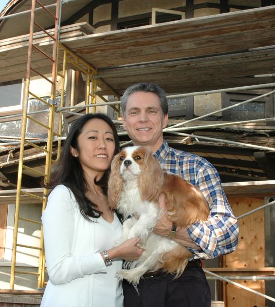 A couple holds a brown and white dog and stands before scaffolding of a construction project