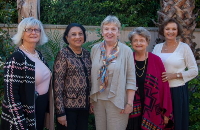 Five women stand together in a line outdoors - all are wearing dressy professional attire
