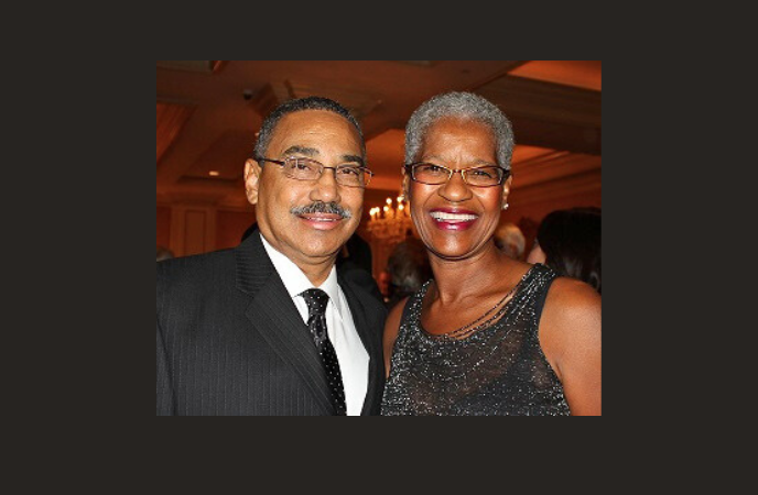 An African American couple stand closely together, they are dressed formally