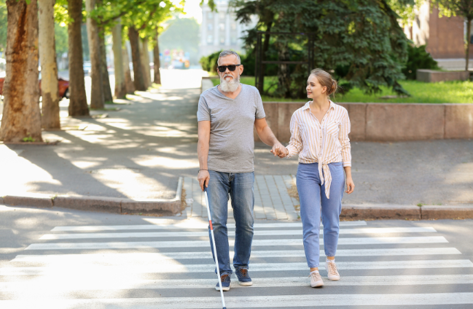 An young woman helped an older blind man who us using a cane to walk through a street crosswalk