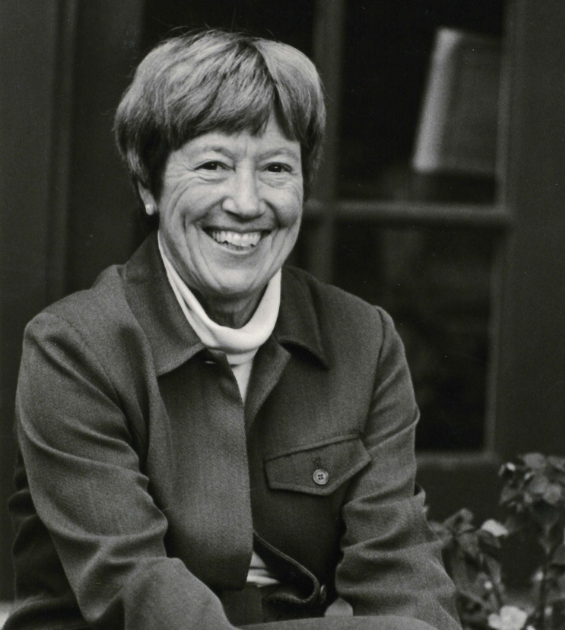 A black and white photo show a woman with short brown hair wearing a jacket and sitting casually