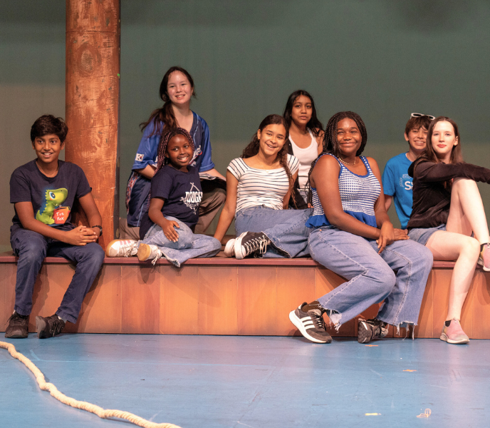 A multiracial group of tweens and teens sits together on a stage set