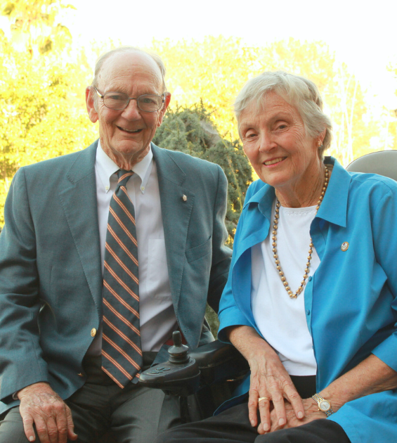 An elderly couple sit together on a bench outdoors