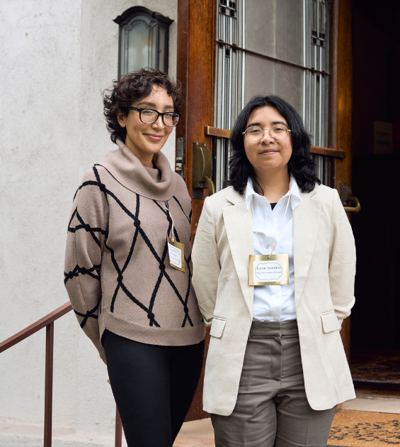 Two young women stand together on stairs with a doorway behind them