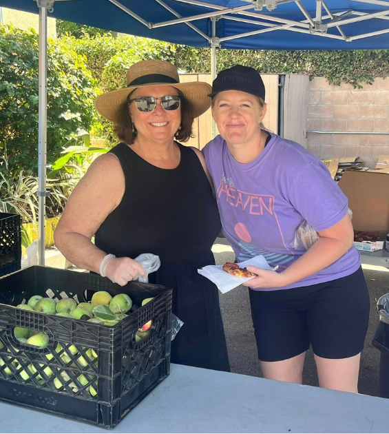 Two woman pose inside a pop up tent and a crate of fruit