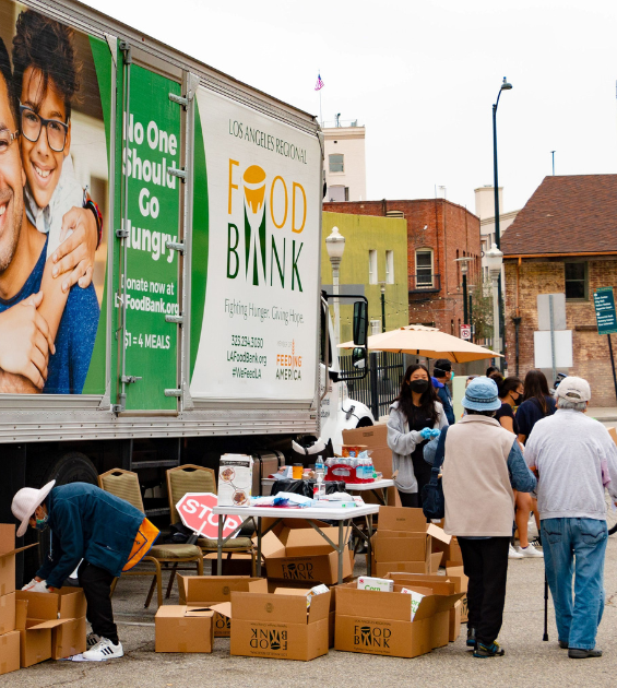 An older couple stroll by a large Food Bank truck - boxes of food are stacked on the ground