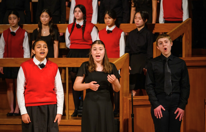 Three teens perform in a choir with several more standing behind them