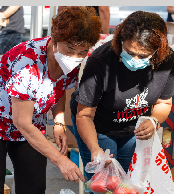 Two women wearing masks choose produce at a food pantry