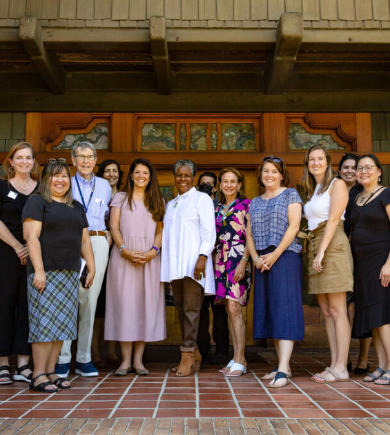 A large group of people pose on a brick porch with beautiful rich colored wood doorway behind them