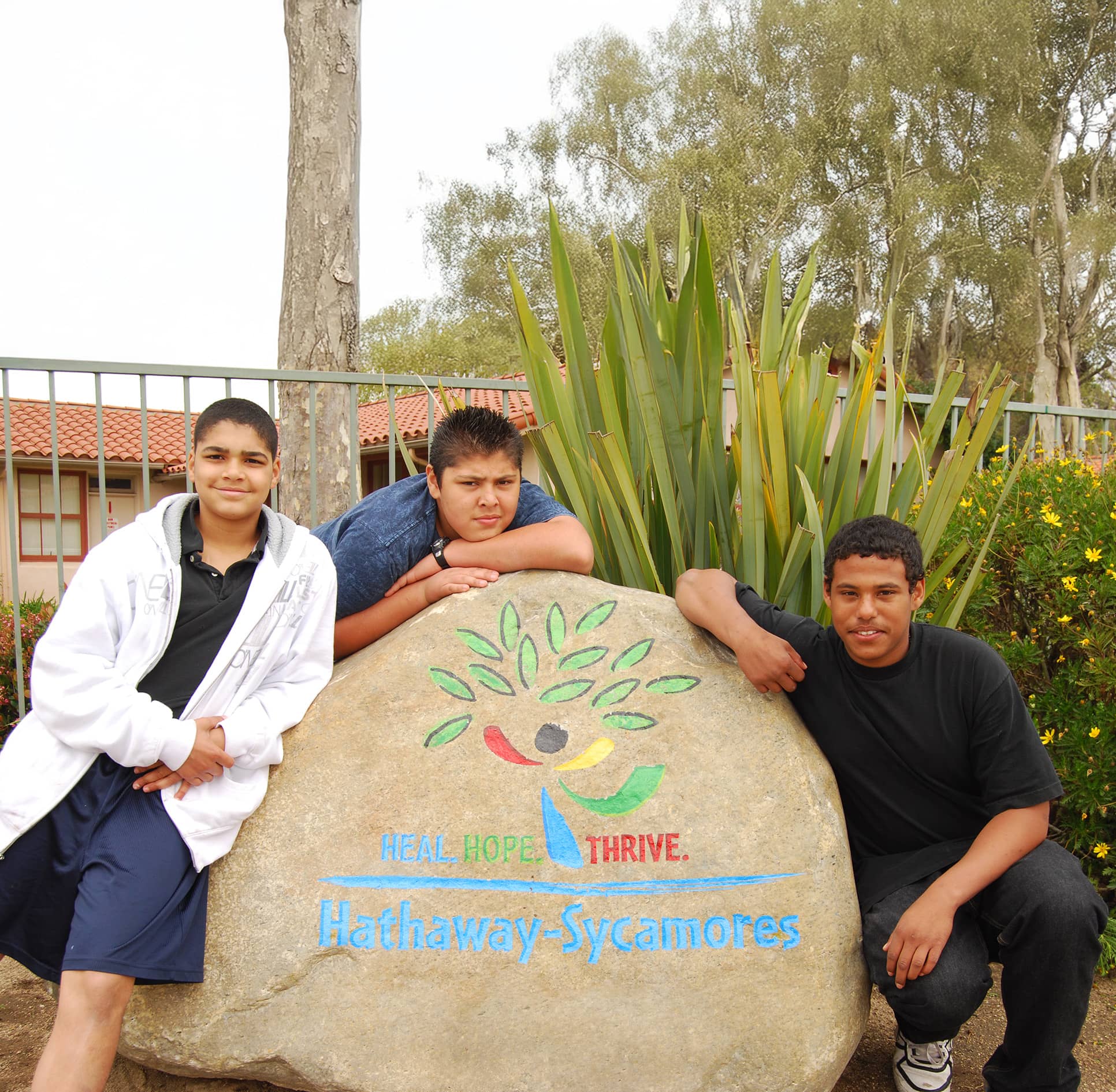 Three young boys leaning against a boulder with logo panted on it
