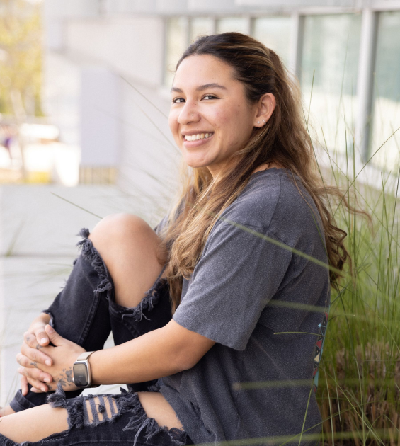 A young woman sits outdoors with her leg up casually