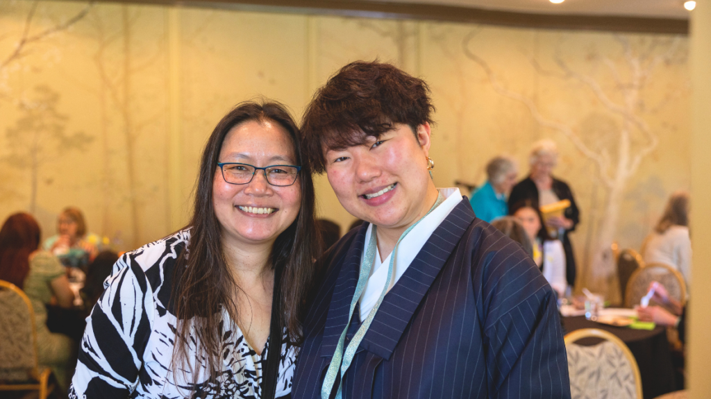 Two Asian women embrace inside a room with other people