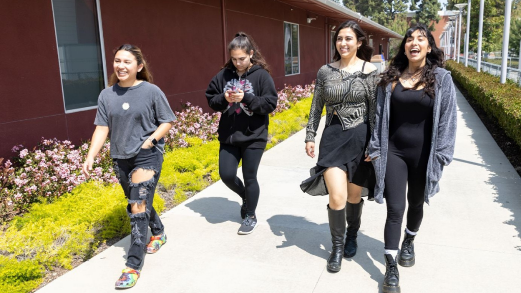Four young women walk together along a sidewalk outdoors