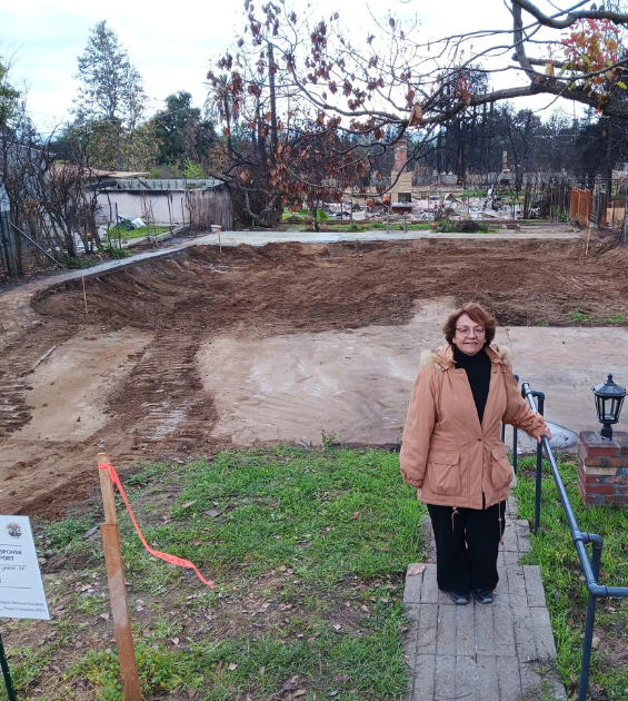 An older woman stands on her cleared lot following the Eaton Fire
