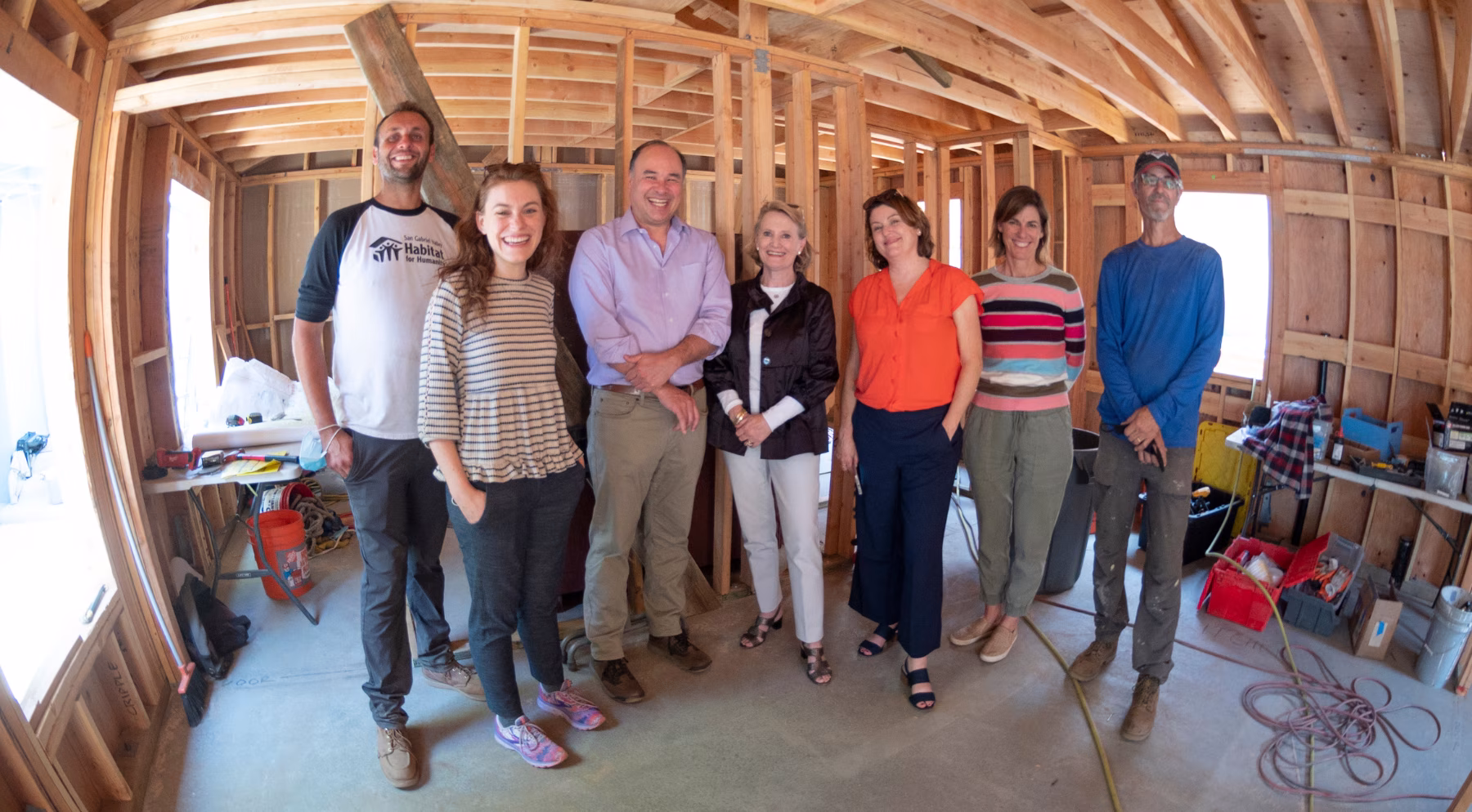 A group of people stand inside a construction site and house being framed