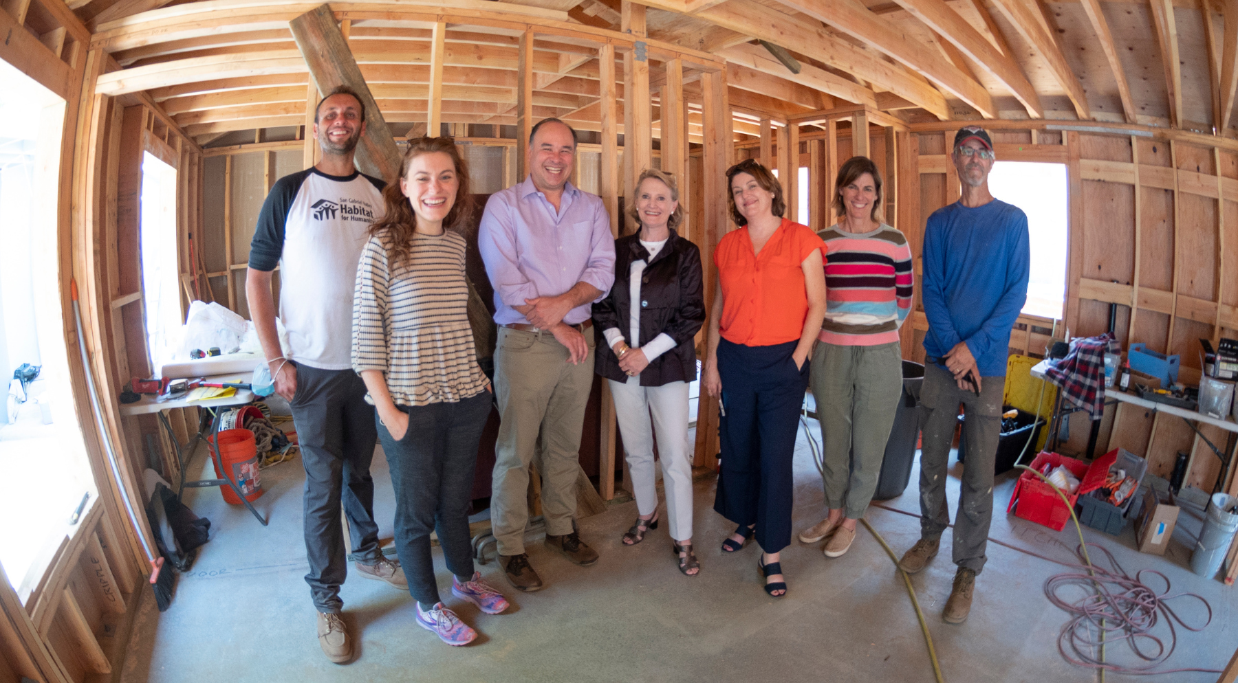 A group of people stand inside a construction site and house being framed