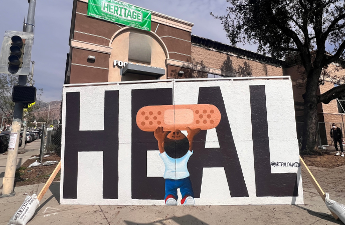 An oversized sign reads HEAL and has a young boy lifting up an Bandaid.