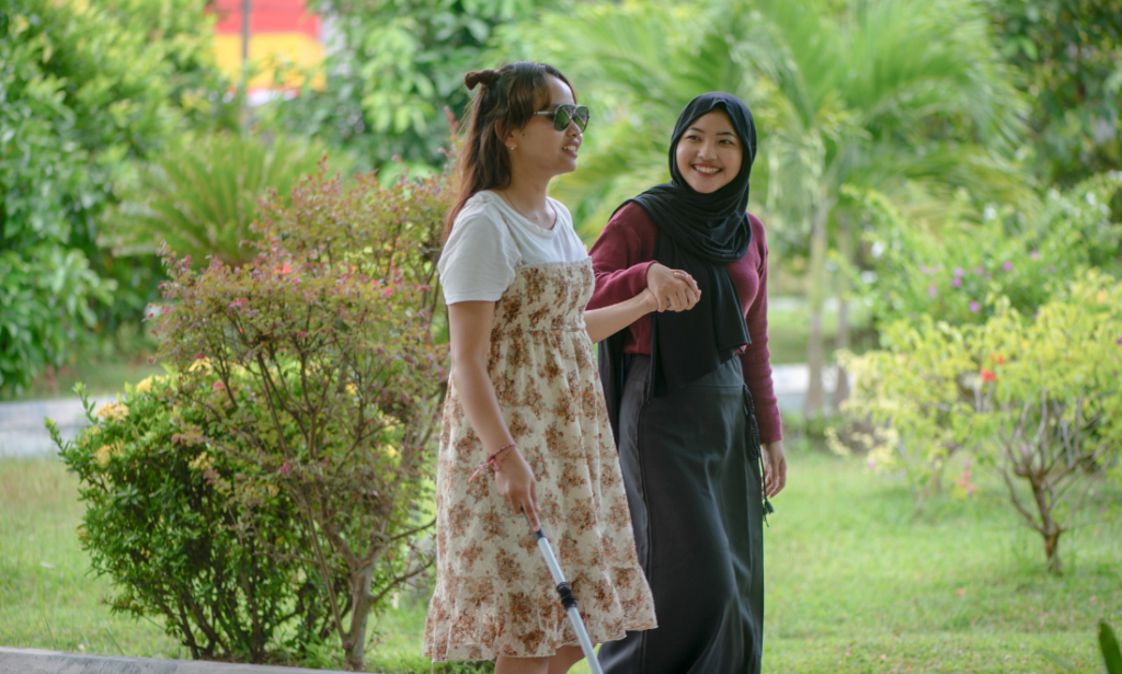 A young blind woman is led by the hand by another young woman