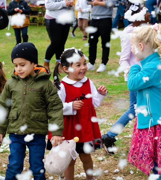 Three children play on grass with falling snow around them