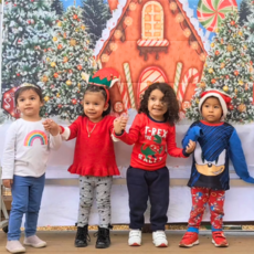 Four young children hold hands and stand in a line before a festive holiday backdrop