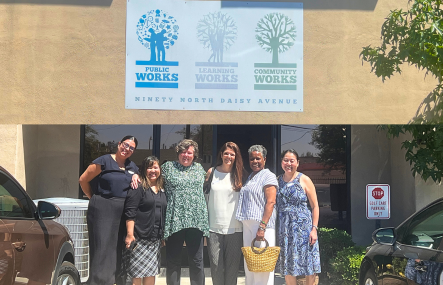A group of six women stand outdoors in front of a building with a sign that reads Learning Works