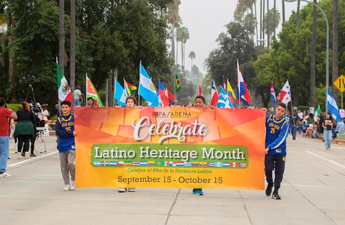 A group of young people march along a street holding many Latin American flags and holding a sign that reads Celebrate Latino Heritage Month