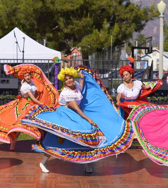 Three women dance wearing vibrantly colored fiestas patrias dresses