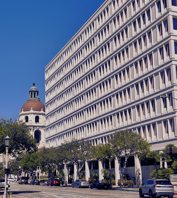 A large white modernist building looms in the foreground with Pasadena City Hall peeking out behind it