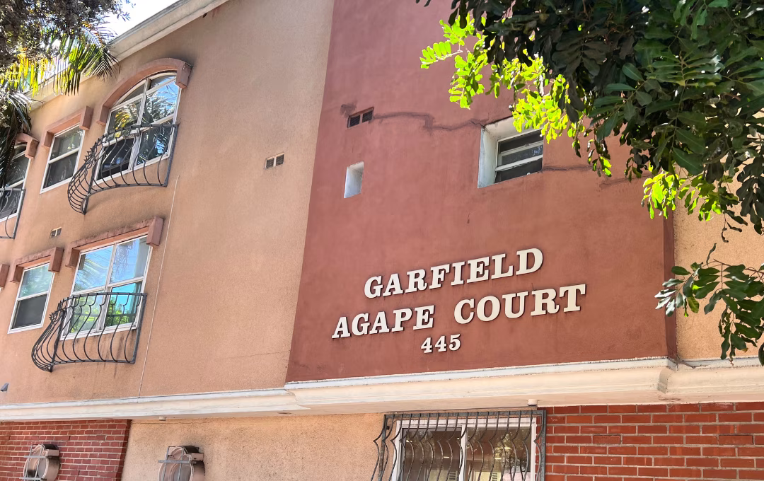 A close up of the exterior red-brick and stucco frontage of an apartment building that says Garfield Agape Court and the address numbers 445 below it
