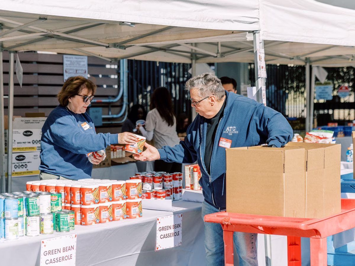 A woman hands a man a canned good from a display of many canned goods at a food drive