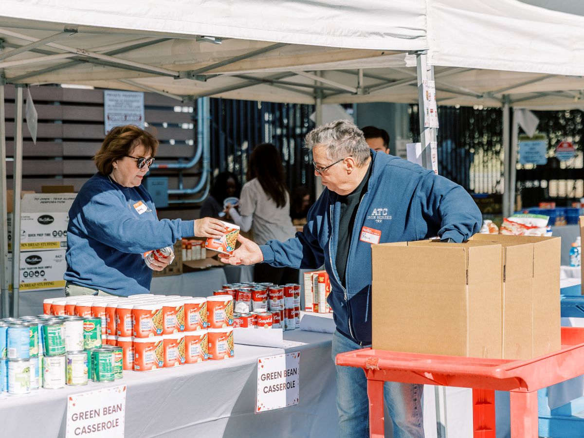 A woman hands a man a canned good from a display of many canned goods at a food drive