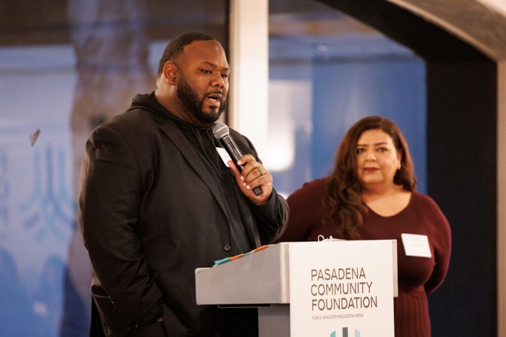 Two adults - a man and woman - stand at a podium while speaking. The sign on the podium says Pasadena Community Foundation