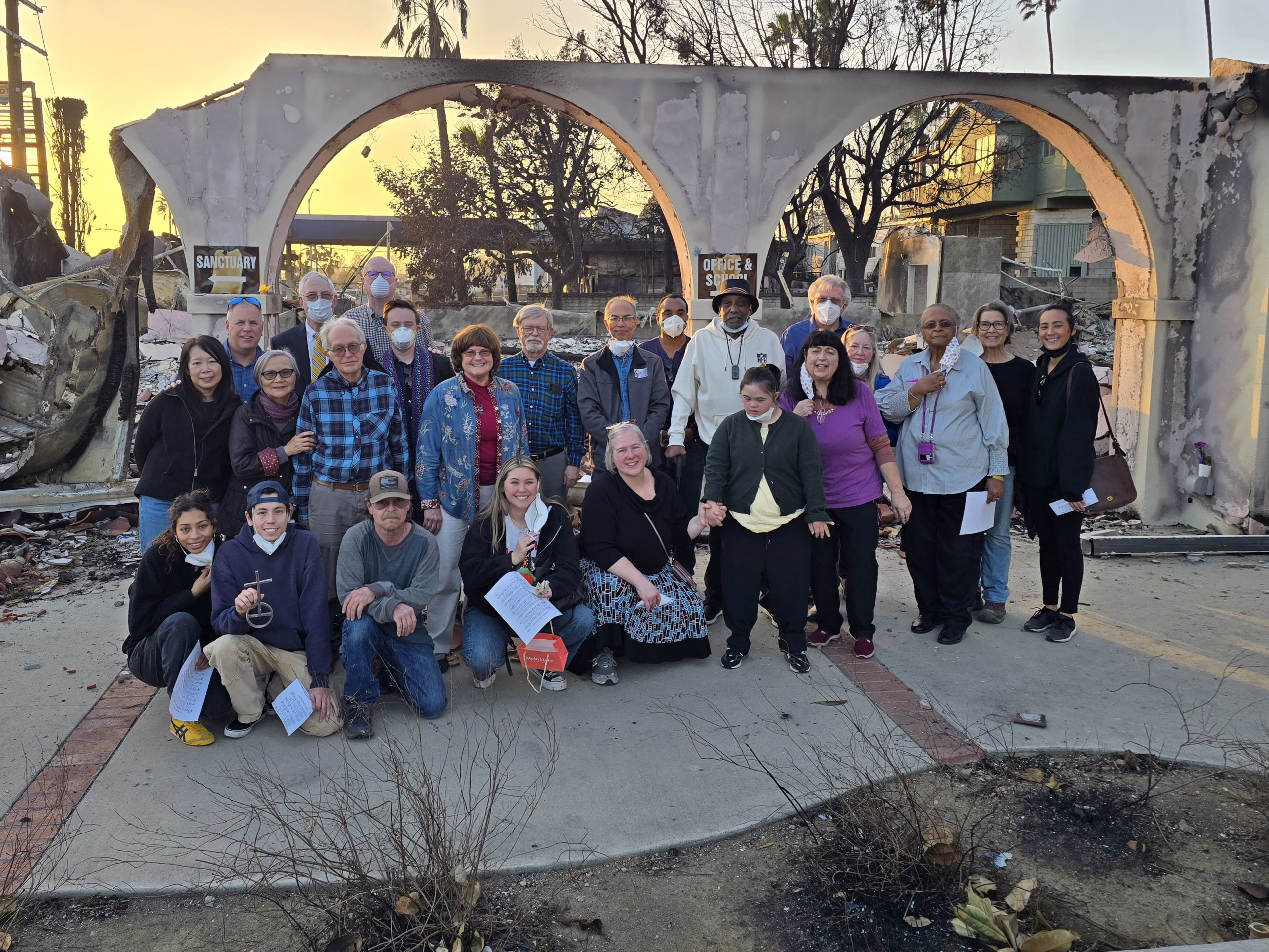 A large group stands in front of a burned out church following the Eaton Fire in Altadena CA