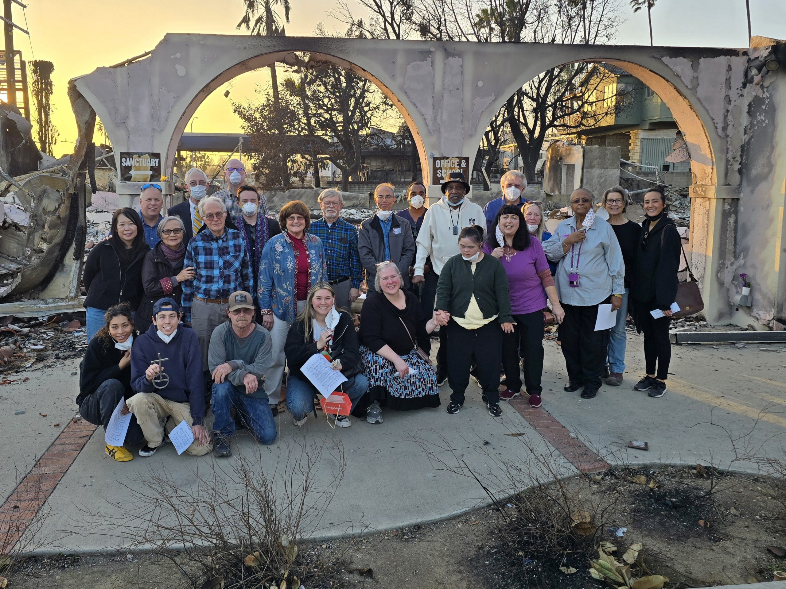 A large group stands in front of a burned out church following the Eaton Fire in Altadena CA