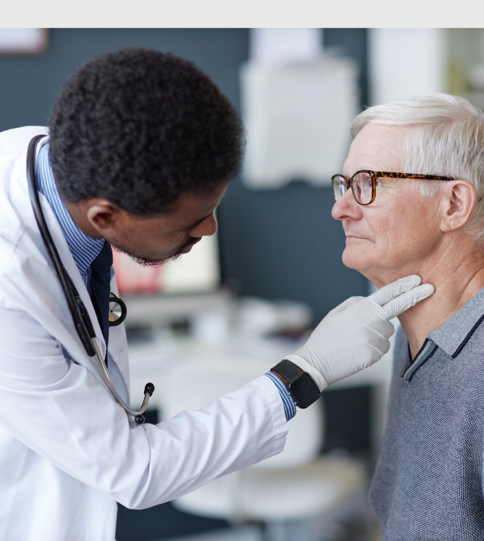 An African American doctor in a white coat and stethoscope exams an older anglo mail wearing glasses