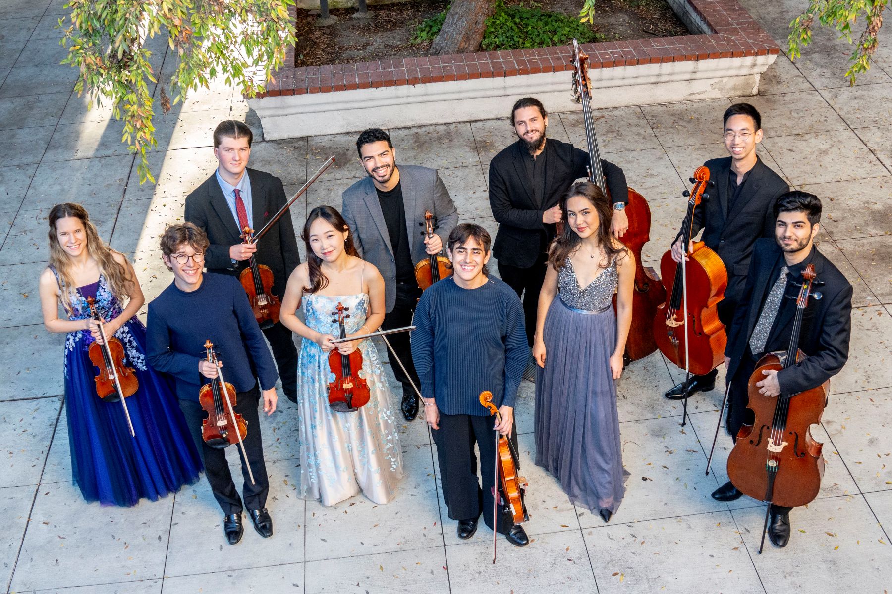 A youth orchestra stands with their instruments, photo taken from above.