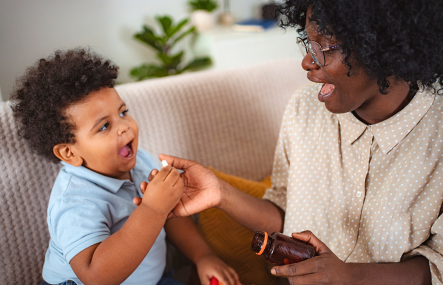 An African American woman smiles and hands a young African American boy some medication