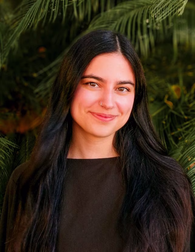 A woman in a black shirt is smiling. Green leaf background.